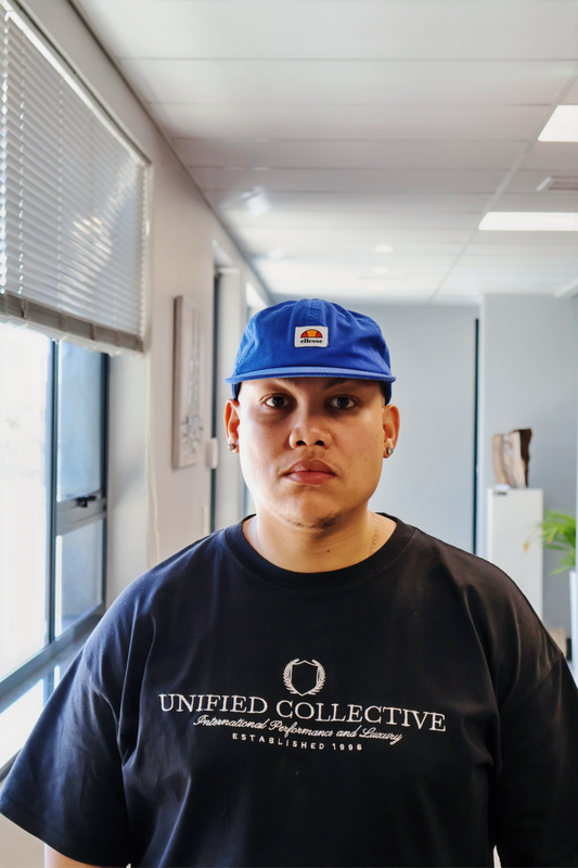 A man in a black shirt with a blue cap. in a office Infront of a camera 